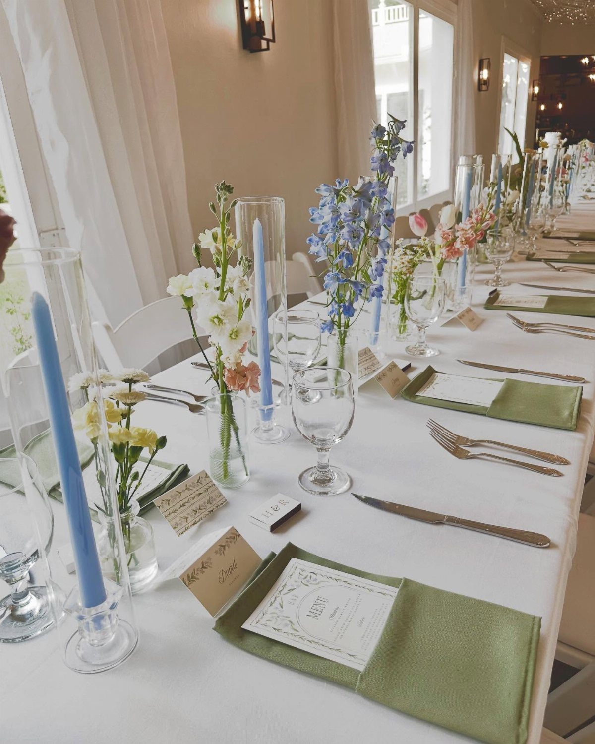 Small glass bud vases with colorful wildflowers and tall blue candles on a wedding reception table.