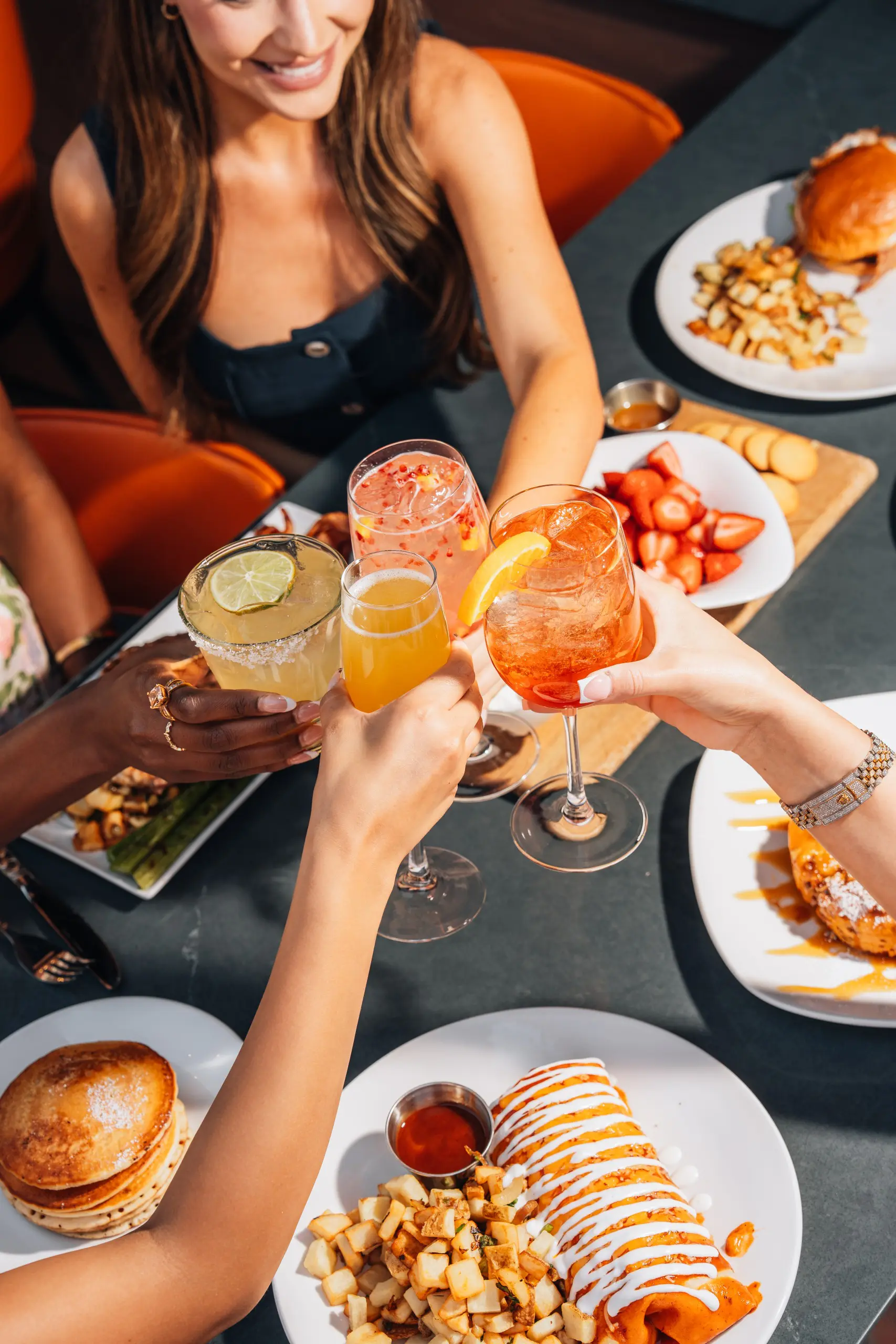 A group of friends gathered around a table at Kona Grill raise their glasses of for a toast. Each person holds in their
