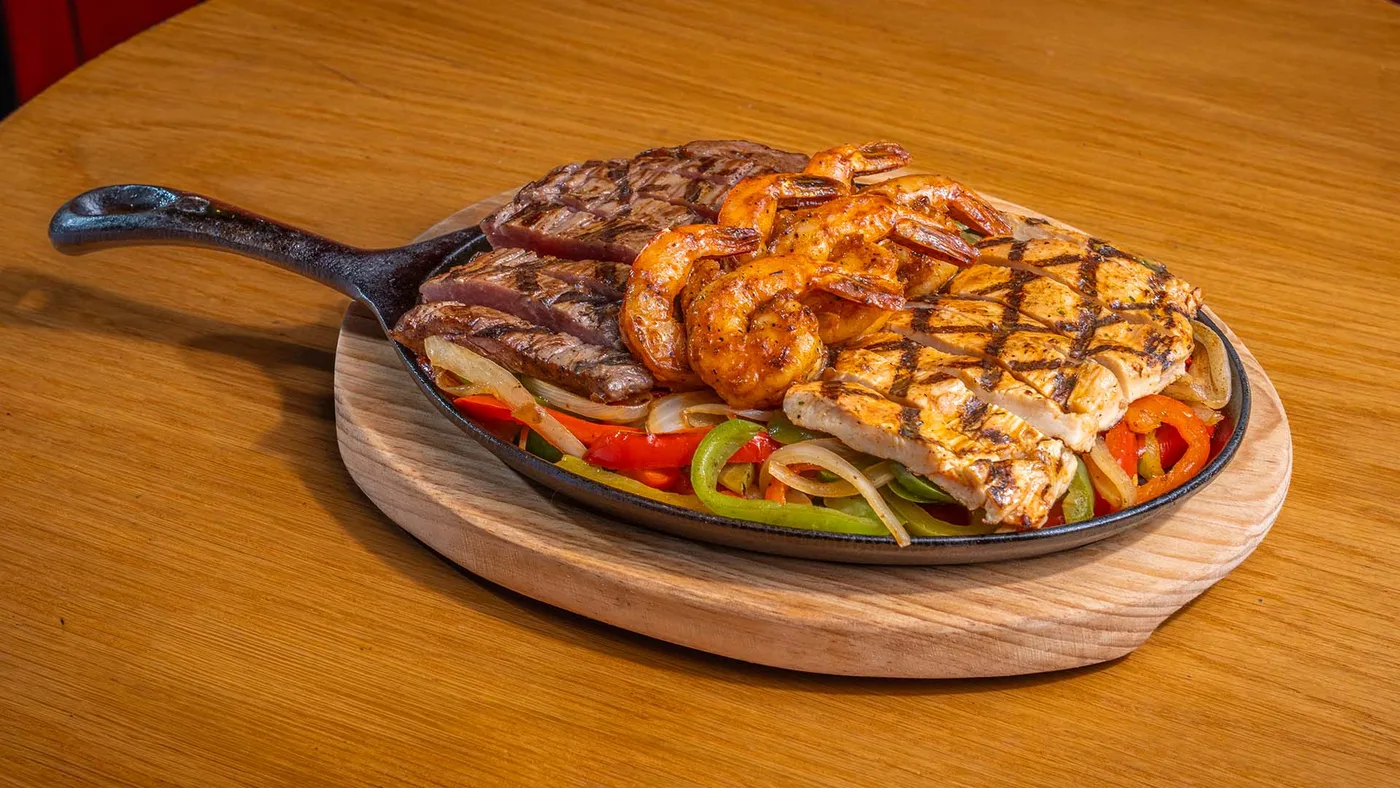Sizzling mixed fajitas with steak, chicken and shrimp on a cast-iron skillet