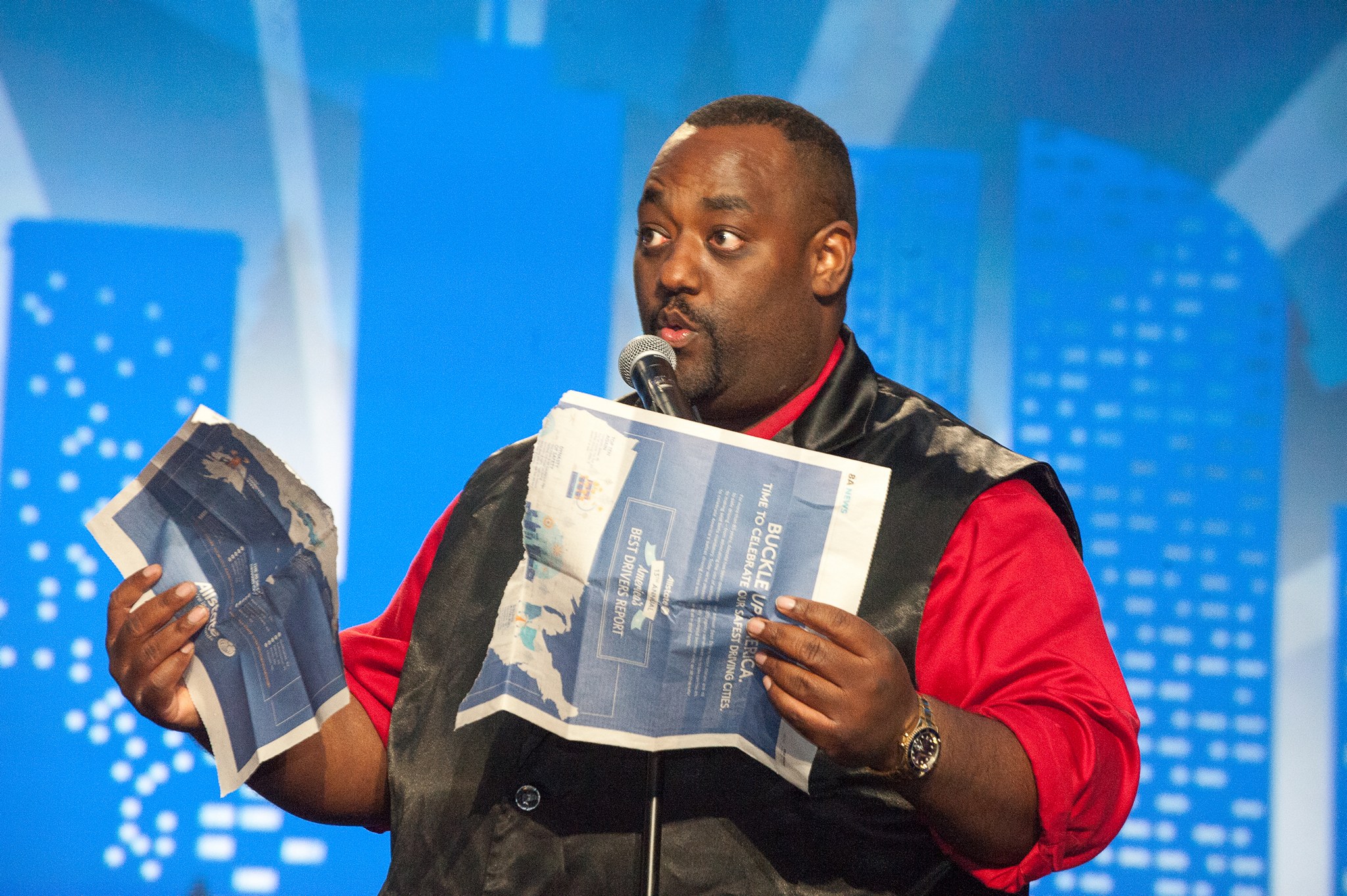 Dewayne Hill performing a newspaper magic trick while speaking into a microphone on stage
