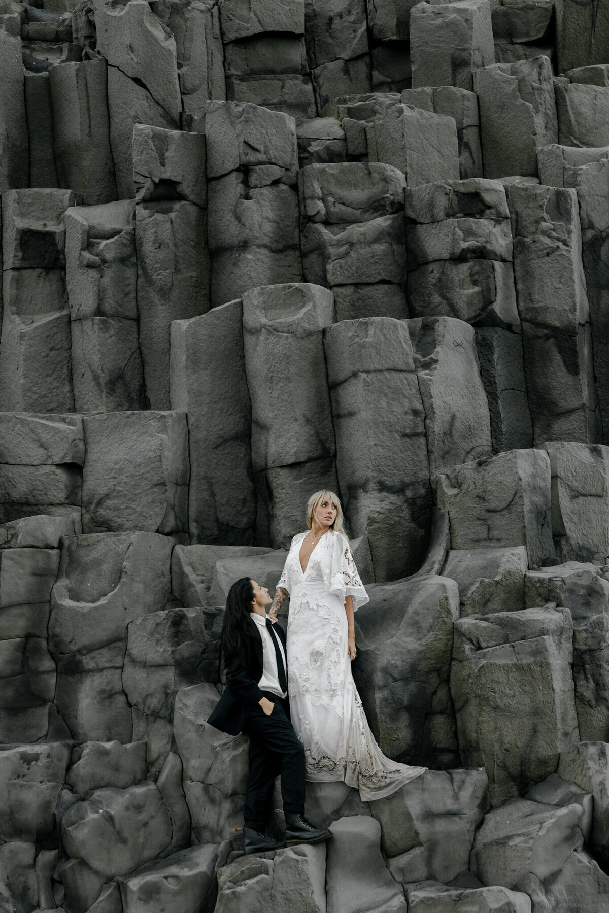 Destination elopement photographer capturing a couple eloping in Iceland, standing together against dramatic basalt rock