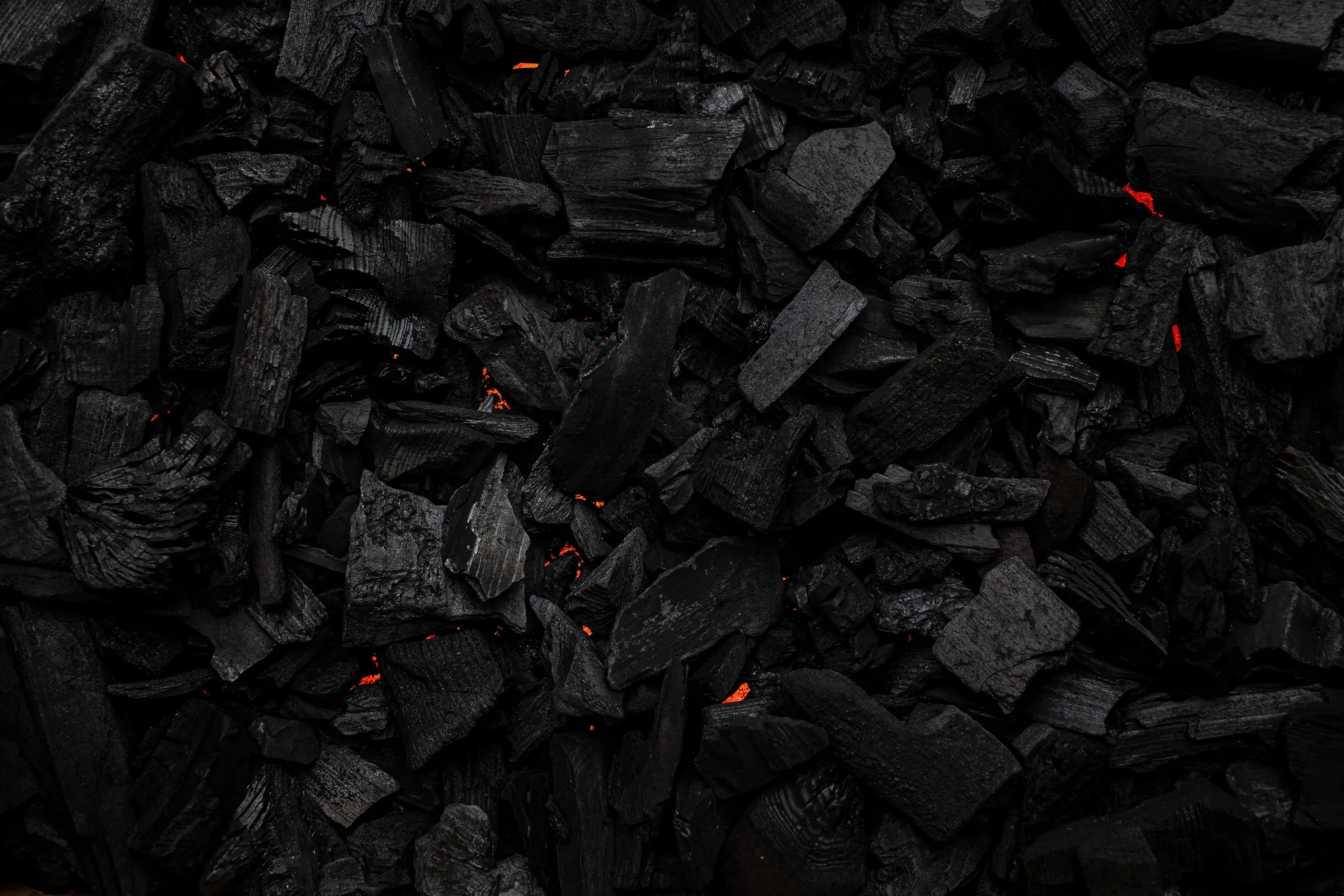Charcoal pieces scattered with faint glowing embers. This image illustrates the raw material used for grilling and barbe