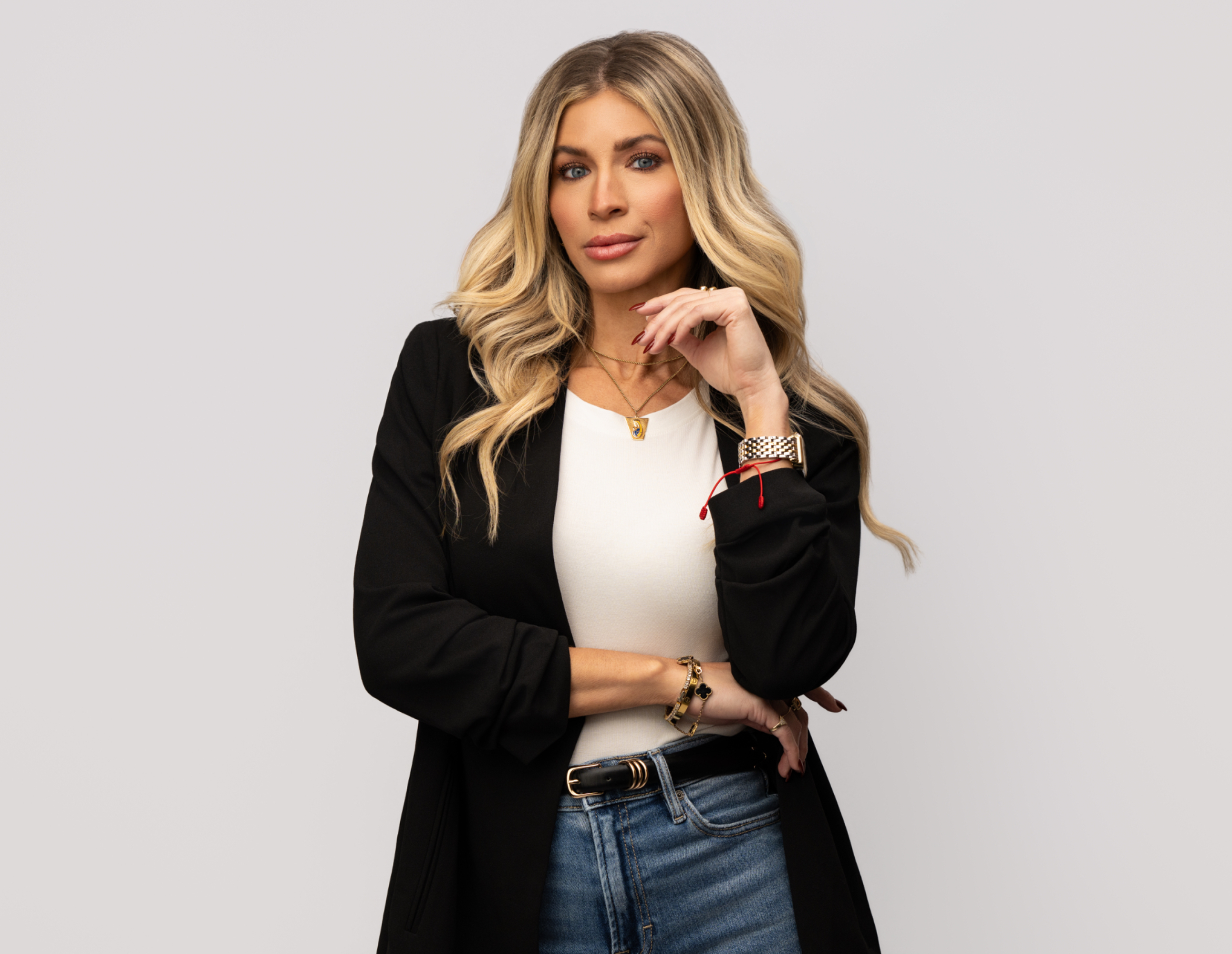 Personal branding portrait of a woman in a black blazer, white top, and jeans against a gray background.