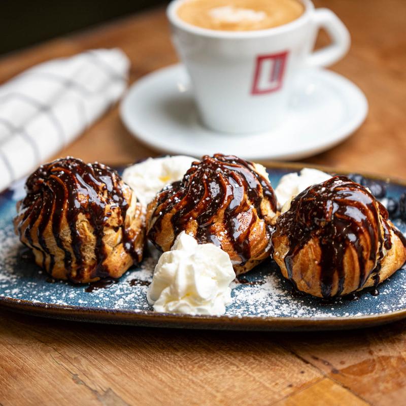 Profiterole plate on a table with a cup of espresso.