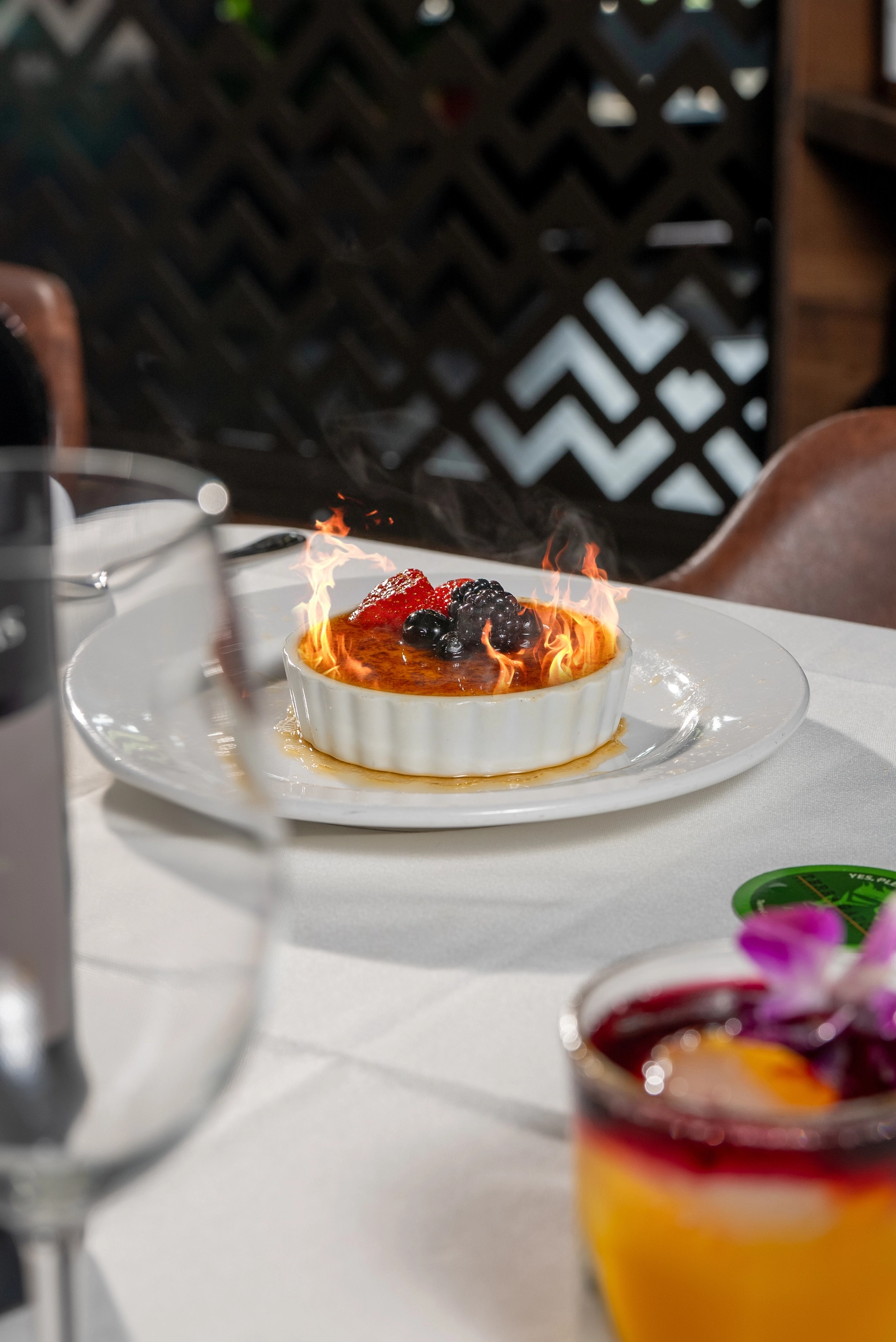 Crème brûlée topped with fresh berries, served in a white ramekin, with flames rising from the caramelized surface.
