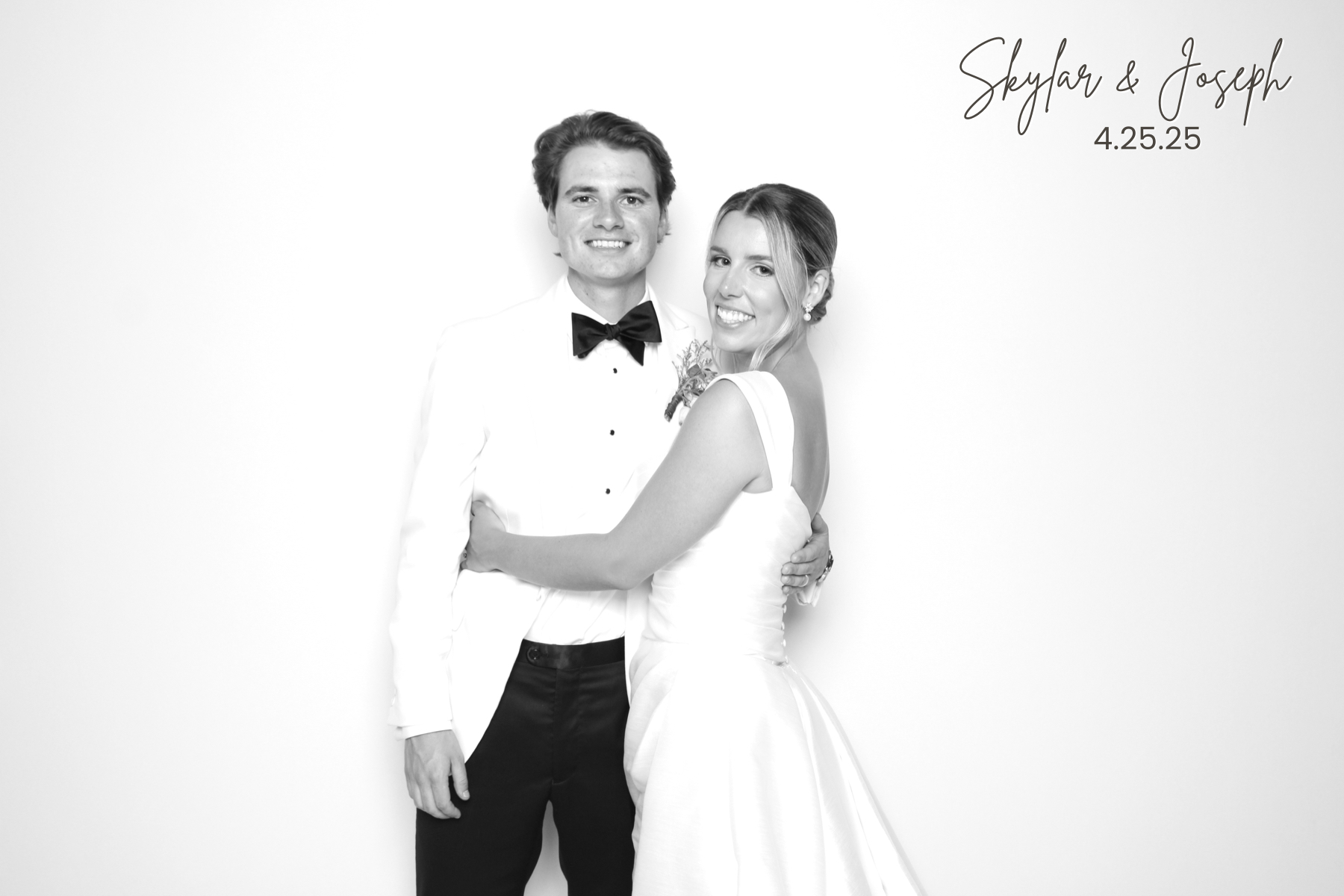 Couple in formal wedding attire smiles together in a polished black-and-white studio portrait.
