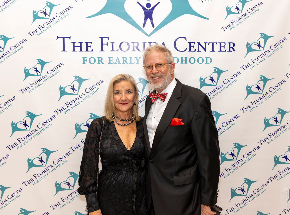 A couple dressed formally poses in front of a backdrop with The Florida Center for Early Childhood logos.