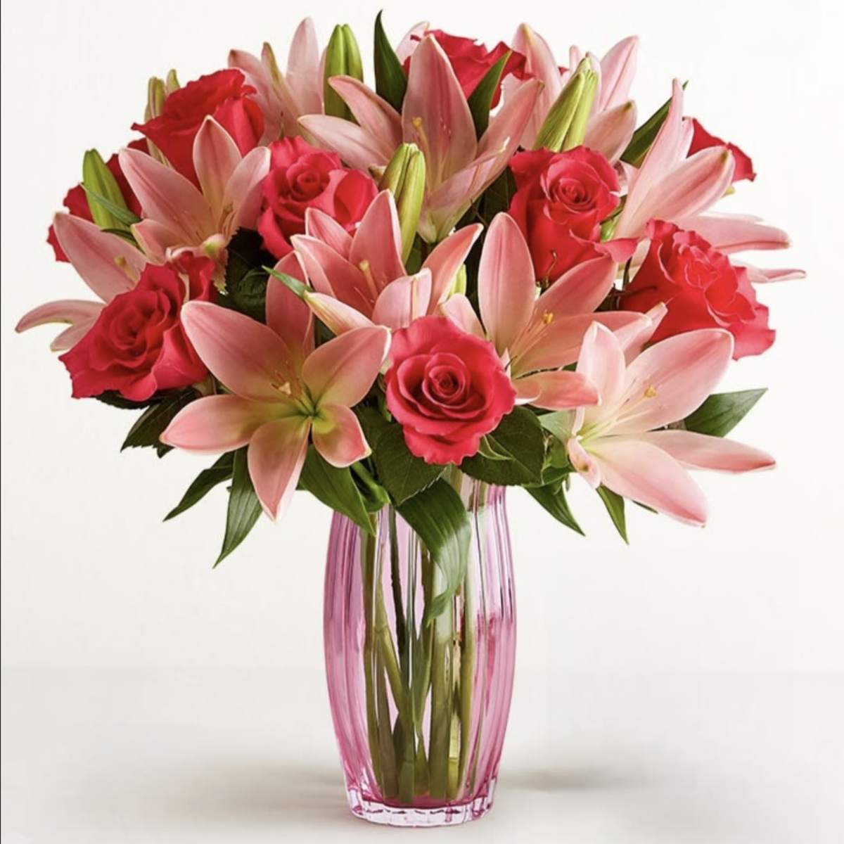 Pink lilies and red roses arranged in a tall glass vase