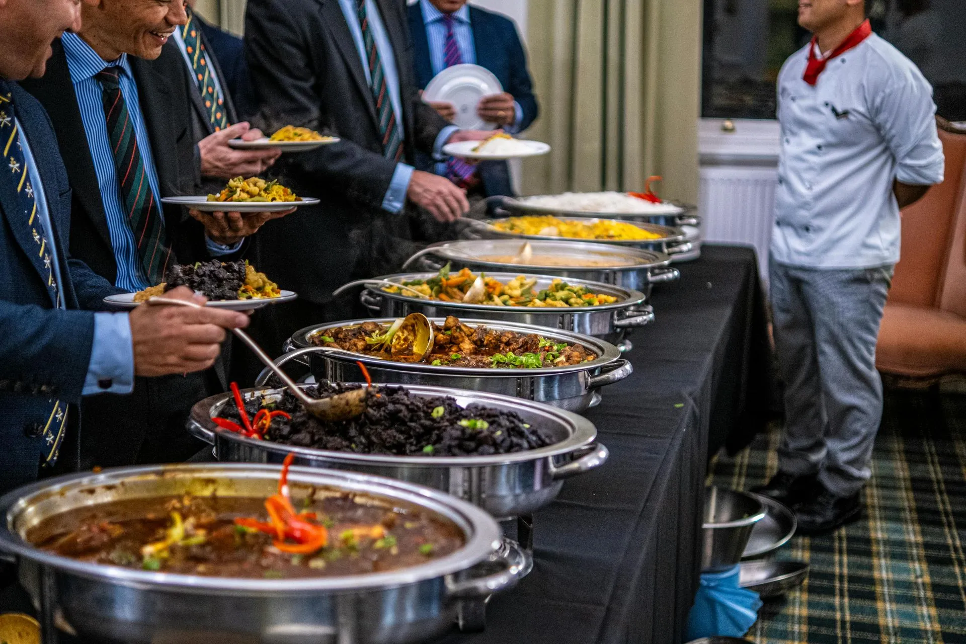 Buffet table with multiple dishes; people serving themselves food at a formal event