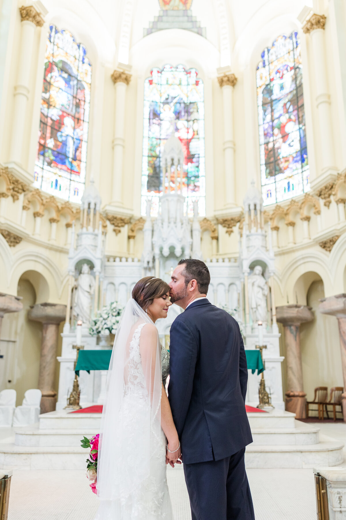 Groom kisses the bride’s forehead at the white marble altar of Sacred Heart Catholic Church in downtown Tampa