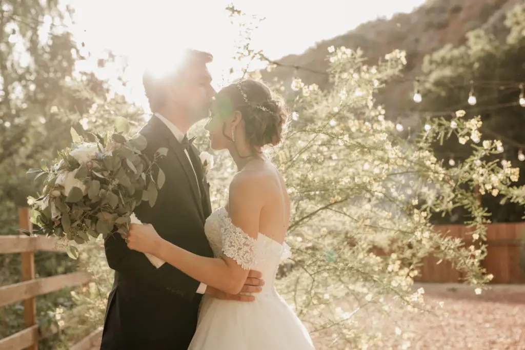 Bride and groom kissing in sunlit outdoor wedding