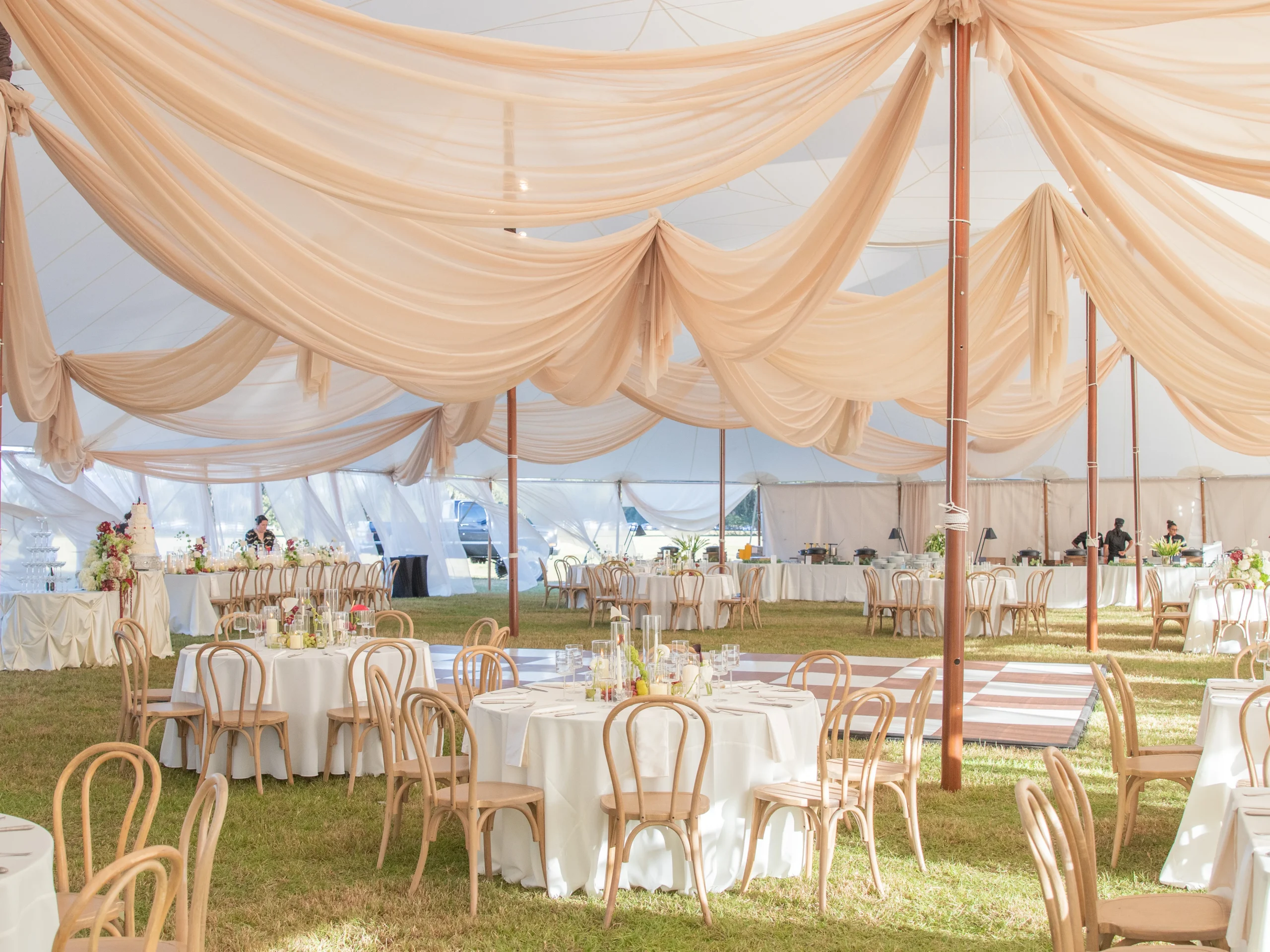 Sailcloth tent wedding setup with champagne fabric draping, blonde bentwood chairs, ivory linens, candle and floral cent