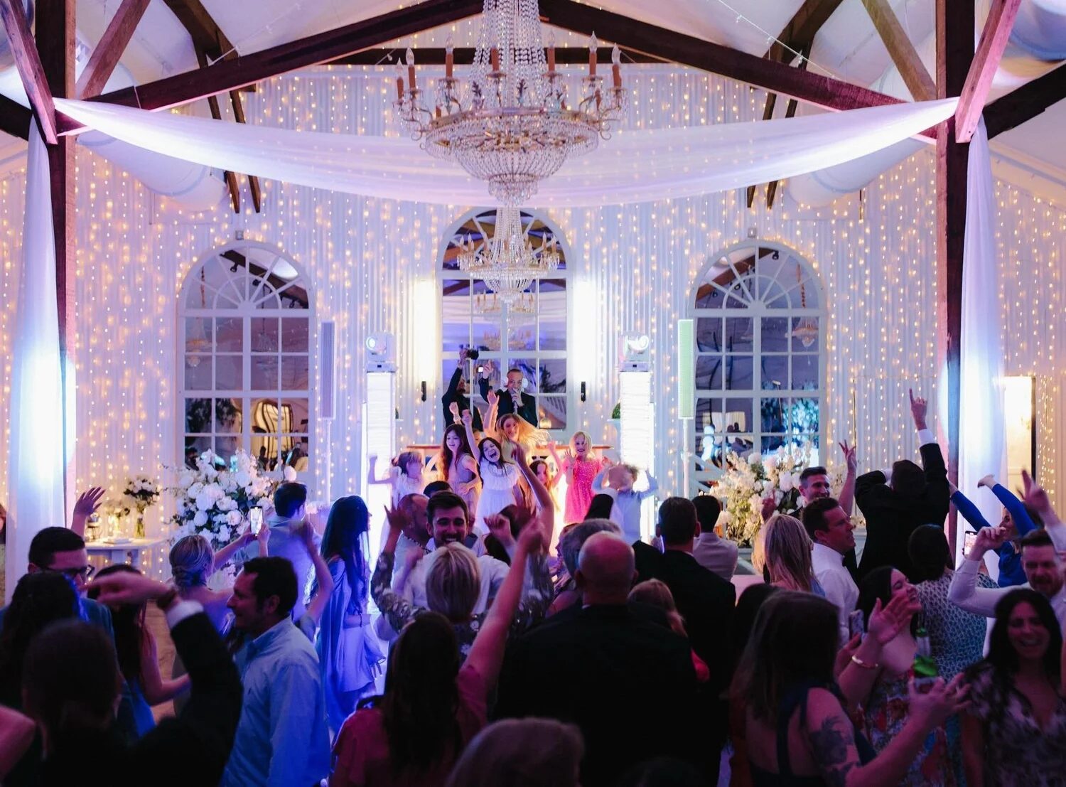 Packed wedding dance floor under chandeliers and cascading string lights