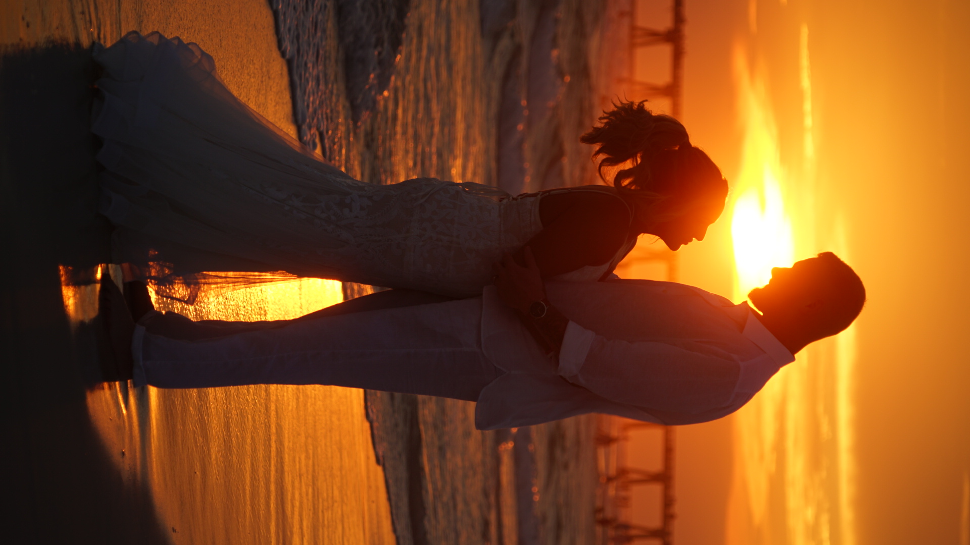 Bride and groom stand at the water's edge on Panama City Beach, arms wrapped as they gaze at each other, their feet