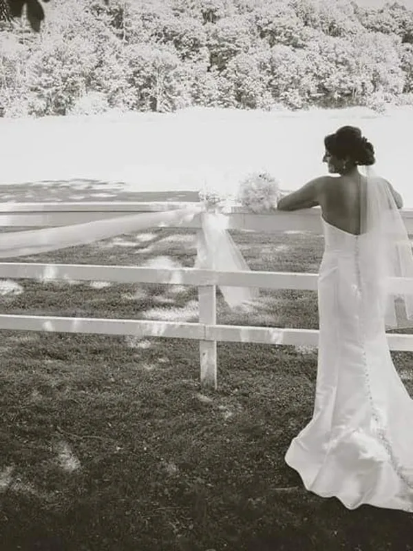Bride in a wedding dress standing by a white fence.