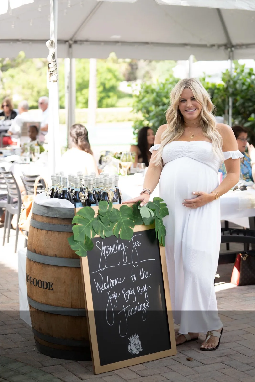 A pregnant woman in a white dress is standing next to a chalkboard.