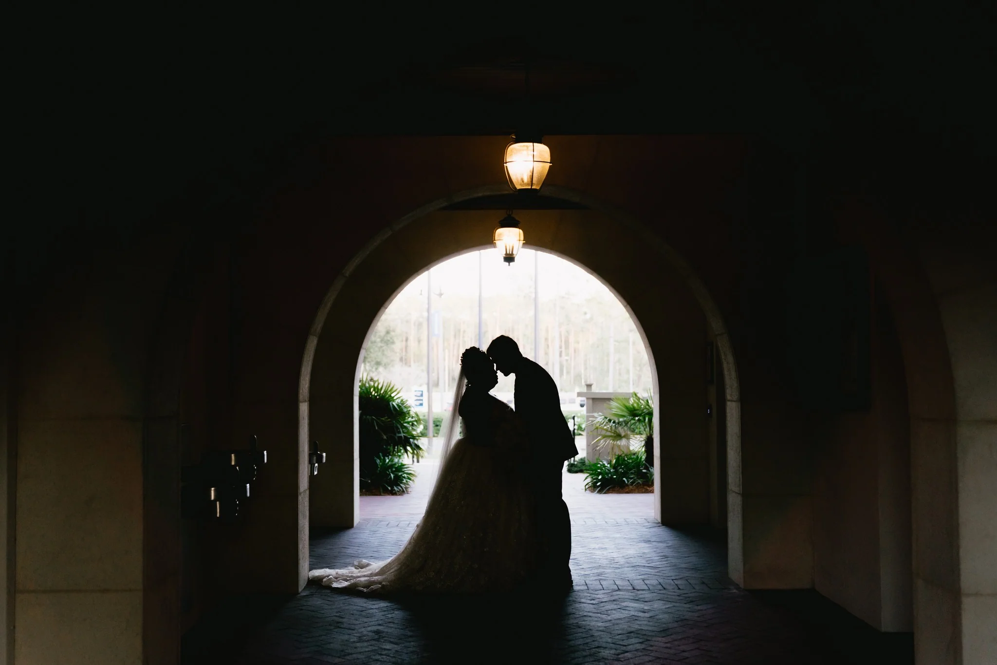 Silhouette of a bride and groom embracing under an archway with warm lighting.